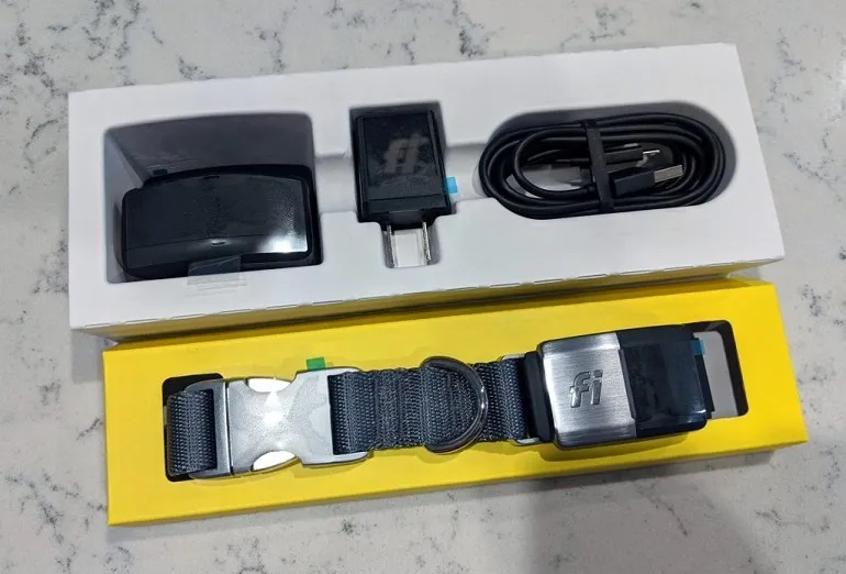Fi smart dog collar kit in an open box, showing the grey nylon collar with the tracking module, charging base, wall adapter, and USB cable