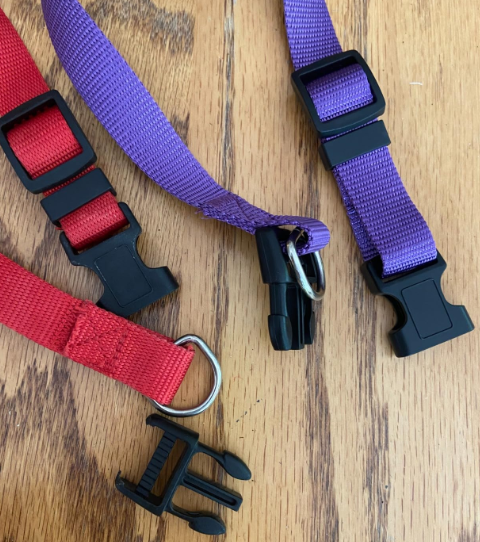 Red and purple best nylon dog collar straps with black buckles and metal D-rings on a wooden floor.