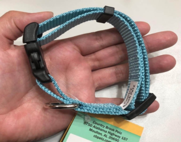 A hand holds an adjustable, light blue nylon dog collar with a black quick-release buckle and an attached product tag.